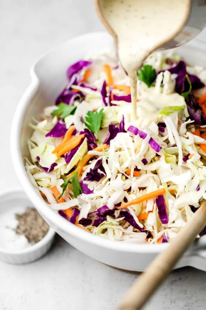 coleslaw dressing being poured onto cabbage
