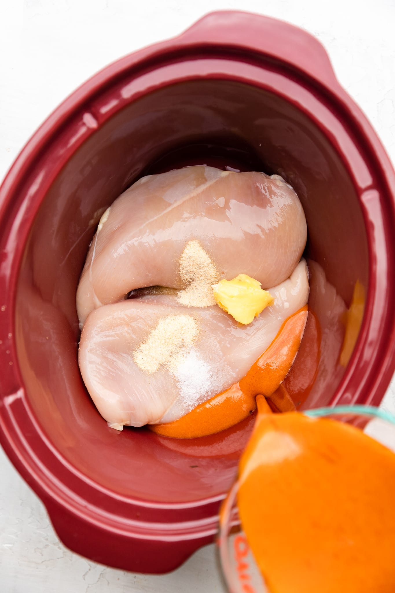 raw chicken in slow cooker with ghee and buffalo sauce