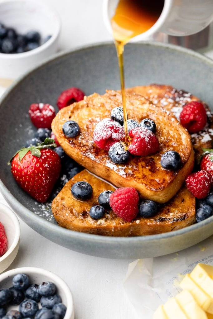 syrup being poured on French toast with berries