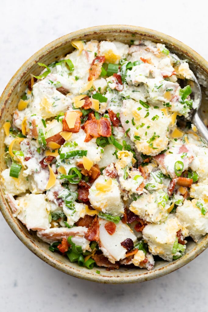 loaded baked potato salad in bowl with spoon