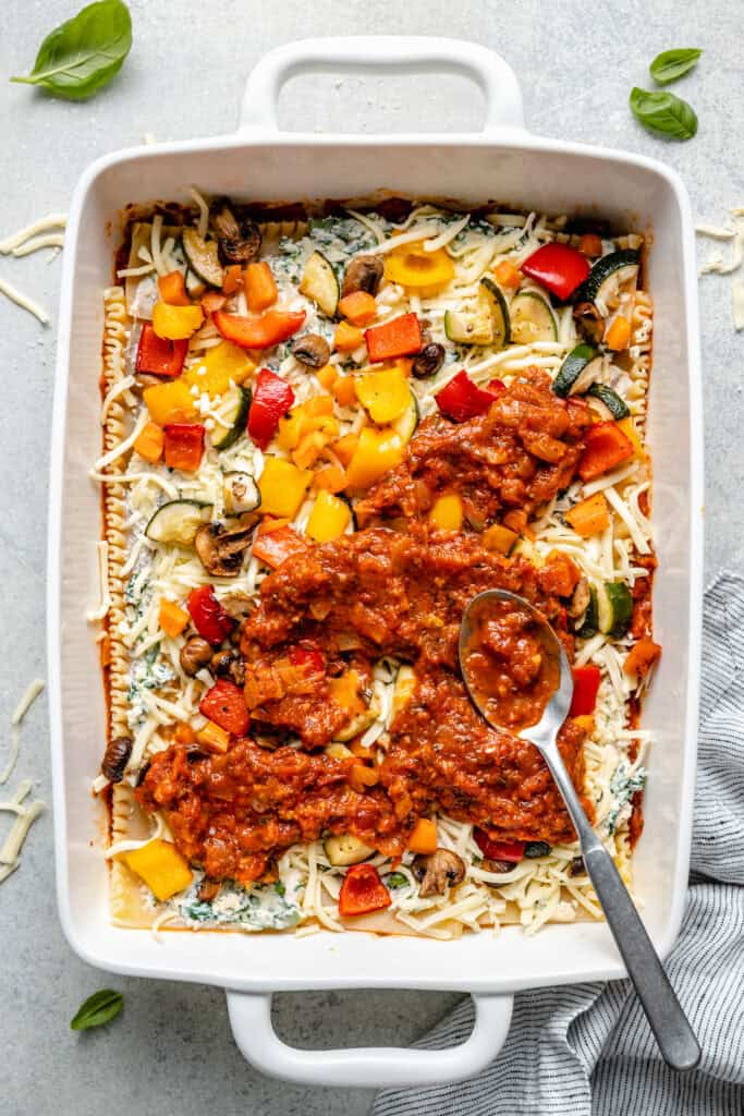 marinara sauce being layered over veggies