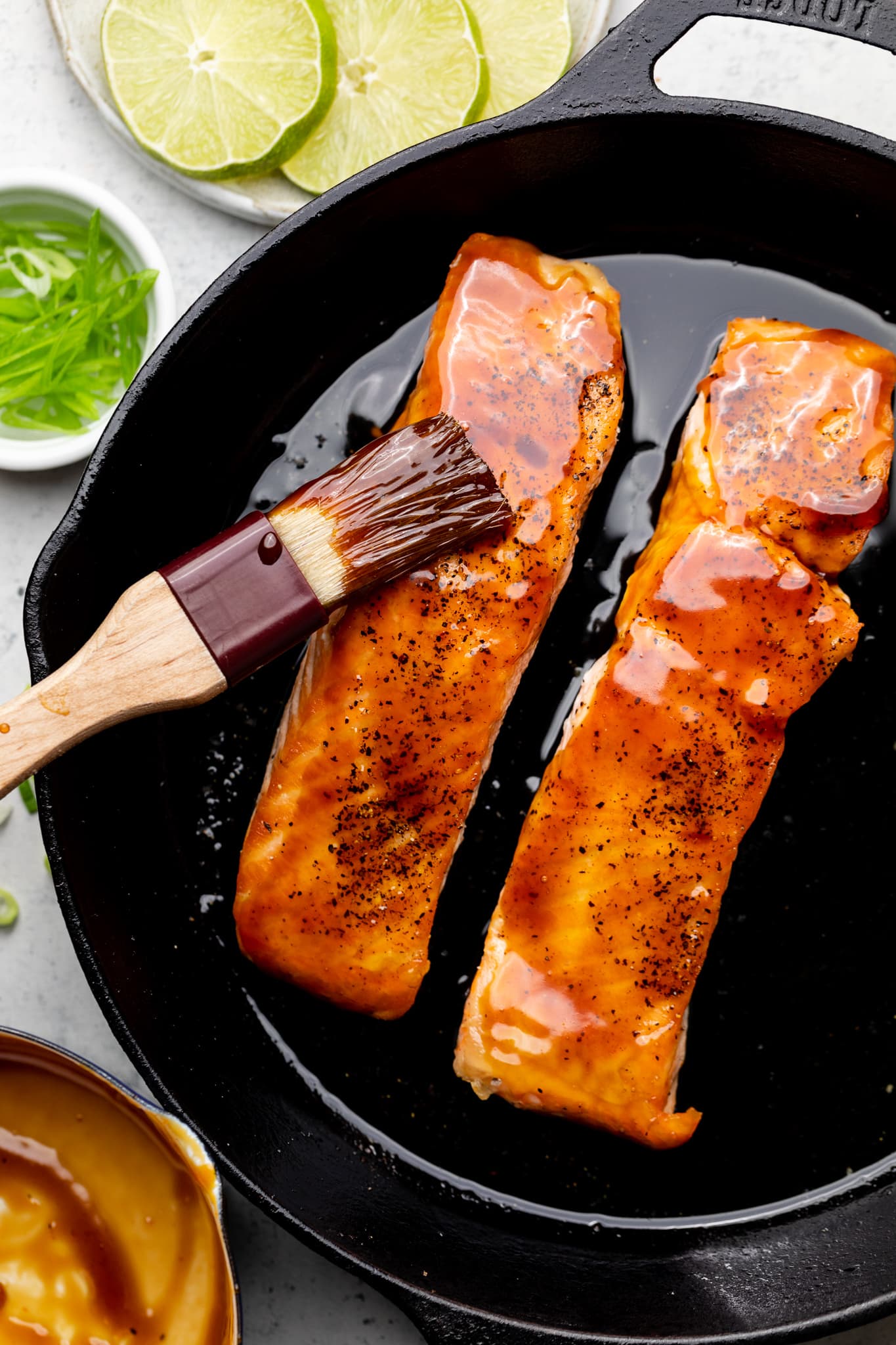 salmon in skillet being brushed with glaze