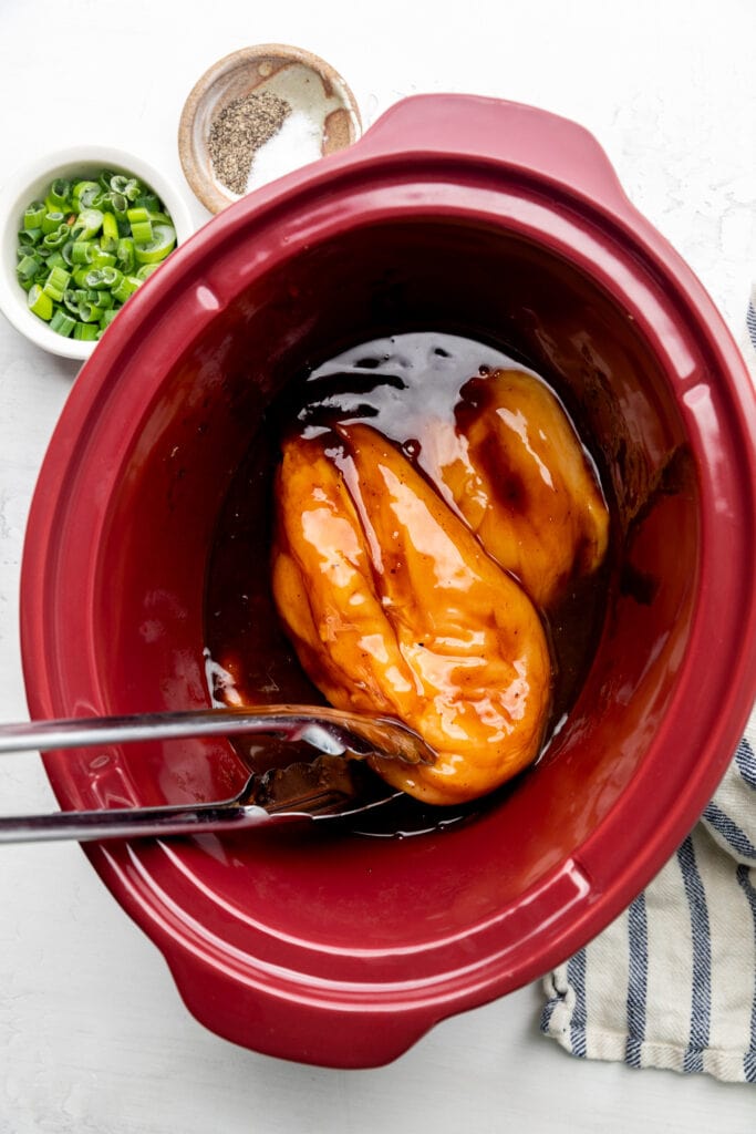 raw chicken breast and barbecue sauce in slow cooker