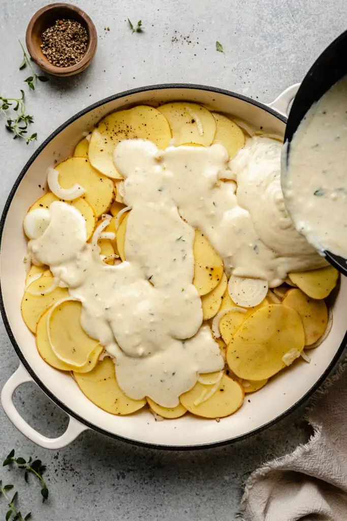 cheese sauce being poured over potatoes