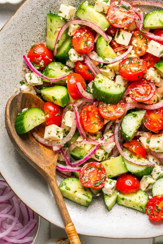 cucumber tomato salad in bowl with wooden spoon