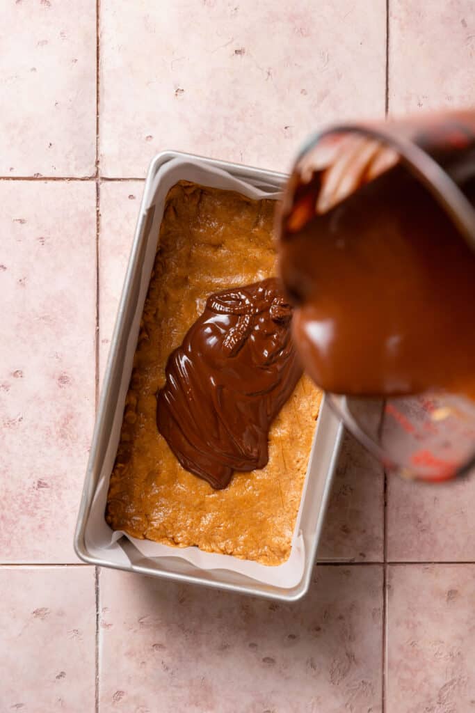 chocolate being poured over peanut butter layer