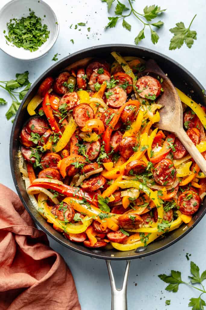 sausage and peppers in skillet with wooden spoon