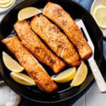 salmon in skillet with lemon wedges