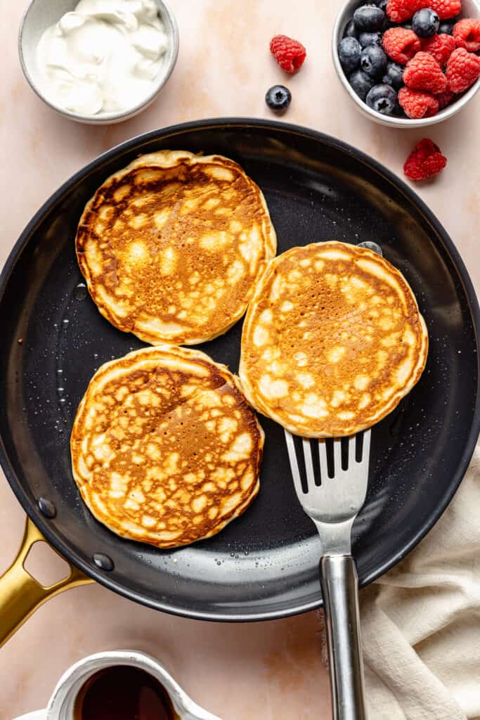 cooked pancakes in black skillet with spatula