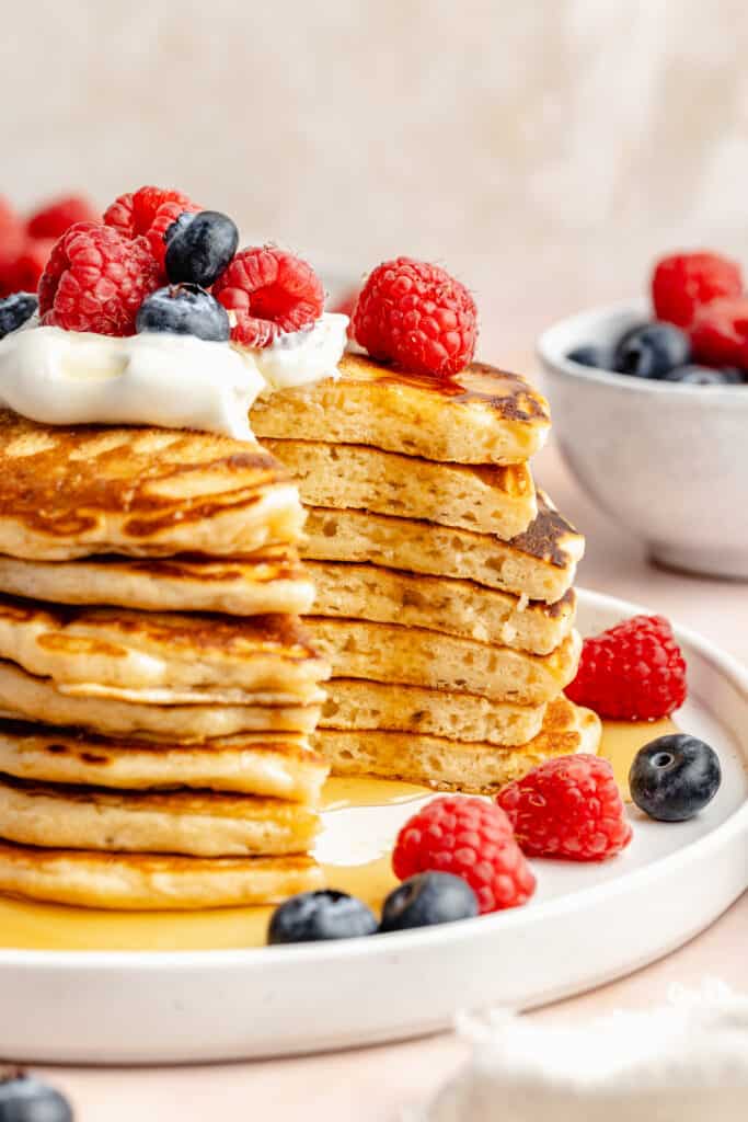 stack of pancakes sliced into topped with berries and whipped cream