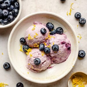 3 scoops of cottage cheese ice cream in bowl topped with blueberries and lemon zest