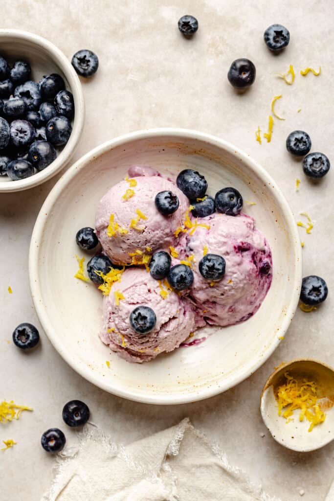 3 scoops of cottage cheese ice cream in bowl topped with blueberries and lemon zest