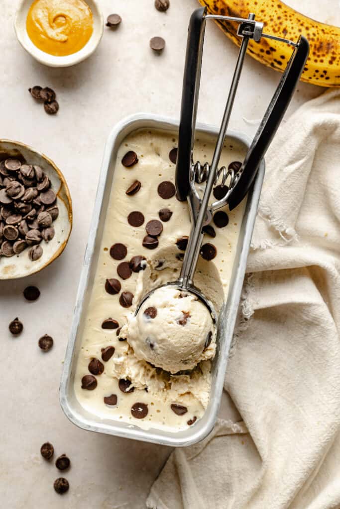 frozen ice cream topped with chocolate chips in loaf pan being scooped with ice cream scoop
