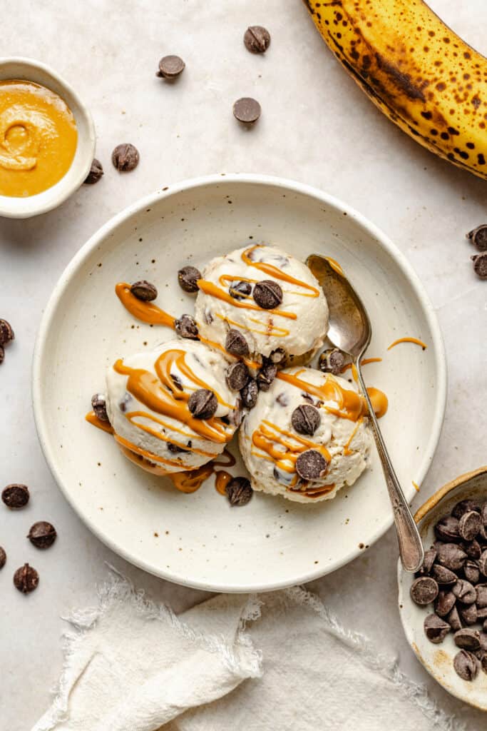 peanut butter banana cottage cheese cream in bowl with drizzle of peanut butter, chocolate chips, and spoon
