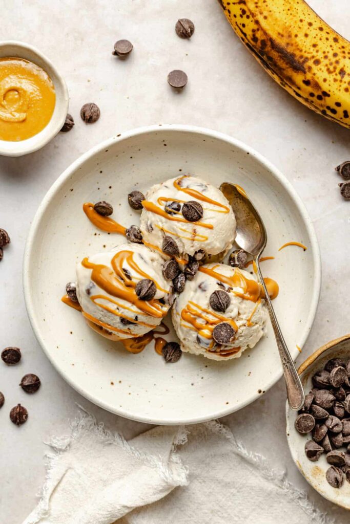 peanut butter banana cottage cheese cream in bowl with drizzle of peanut butter, chocolate chips, and spoon