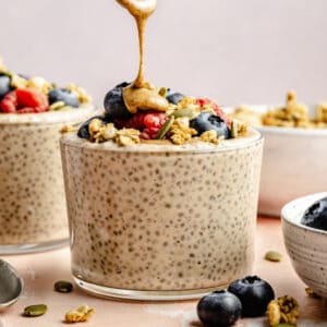 protein chia seed pudding in glass with toppings and nut butter being drizzled on top