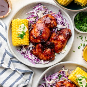 bbq chicken thighs on plates with coleslaw and corn