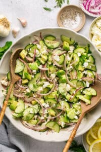 cucumber feta salad in bowl with two wooden serving spoons