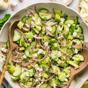 cucumber feta salad in bowl with two wooden serving spoons