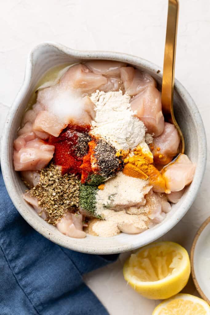 raw chicken, spices, and Greek yogurt in mixing bowl