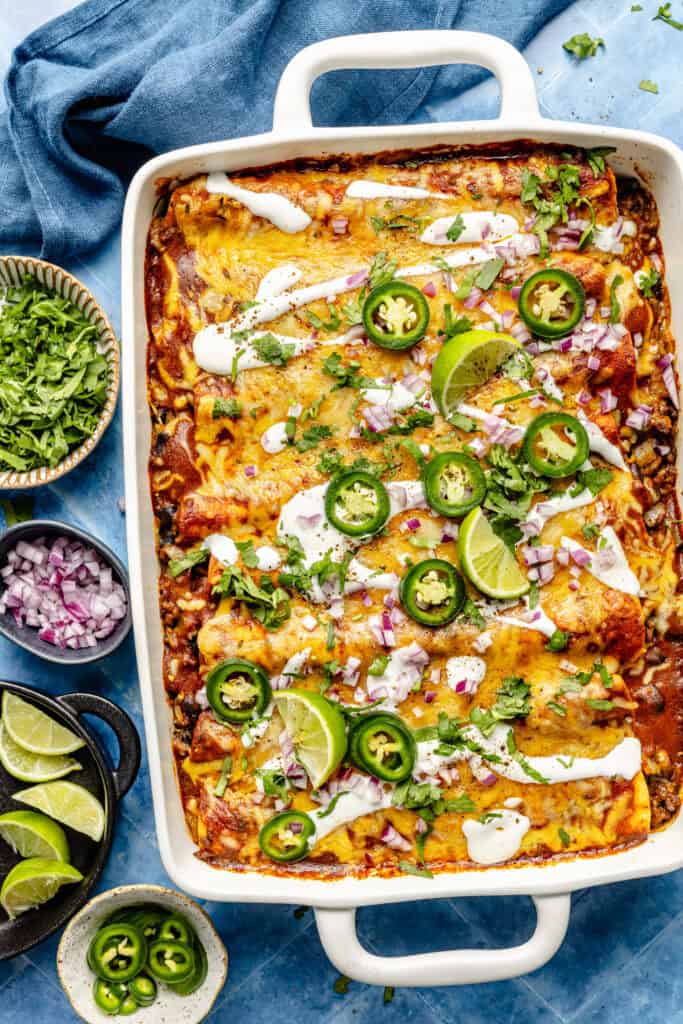 casserole dish of baked beed enchiladas with toppings and small bowls of toppings on the side