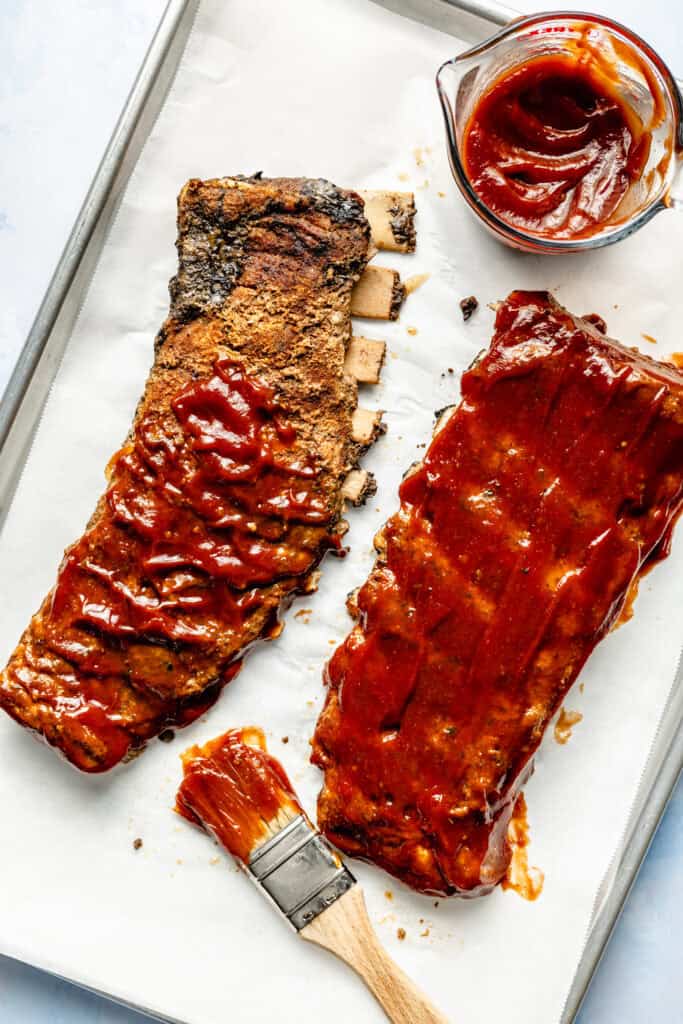 barbecue sauce being spread over ribs