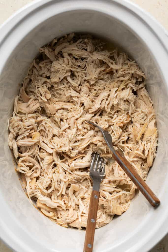 shredded chicken in slow cooker with two forks