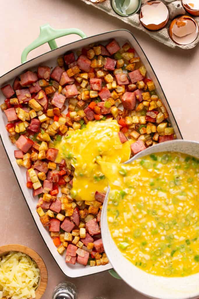 egg mixture being poured over ham and veggies in casserole dish