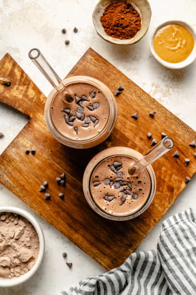 chocolate protein shake in glass with straw on cutting board