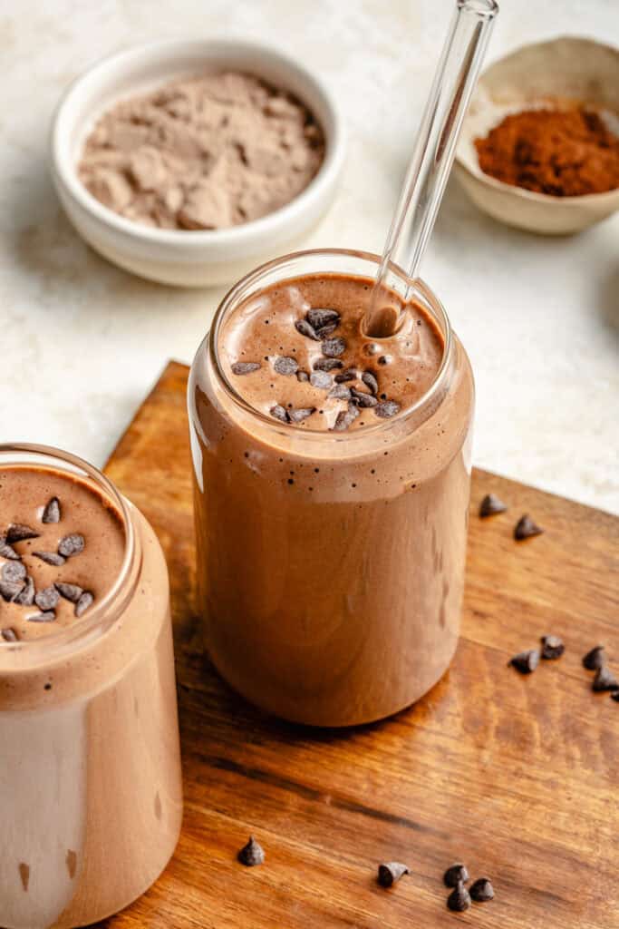 chocolate protein shake in glass with straw on cutting board