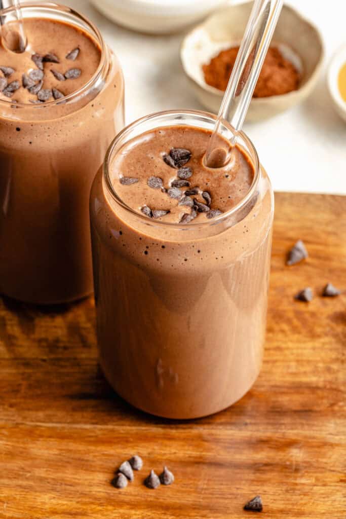 chocolate protein shake in glass with straw on cutting board