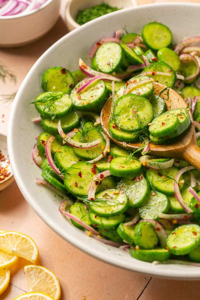 cucumber onion salad in white mixing bowl with spoon