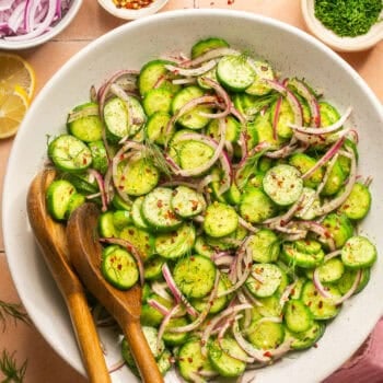 cucumber onion salad in white mixing bowl with wooden serving spoons