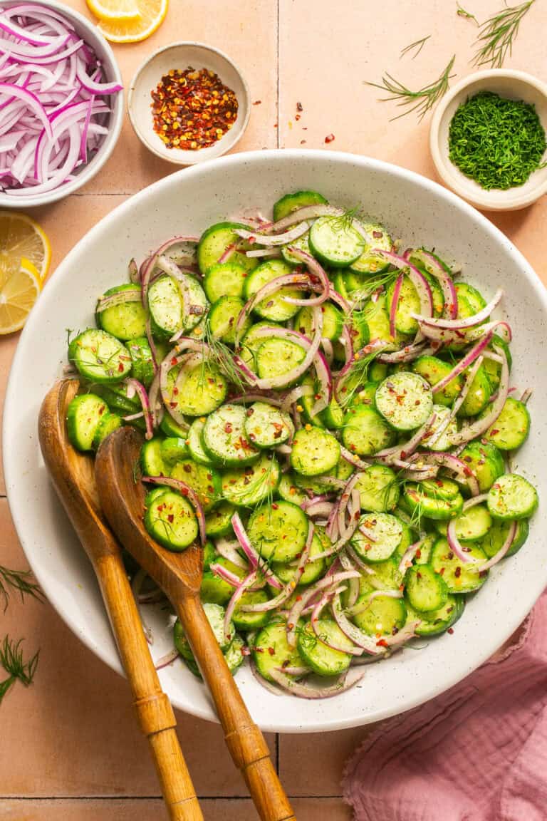 cucumber onion salad in white mixing bowl with wooden serving spoons