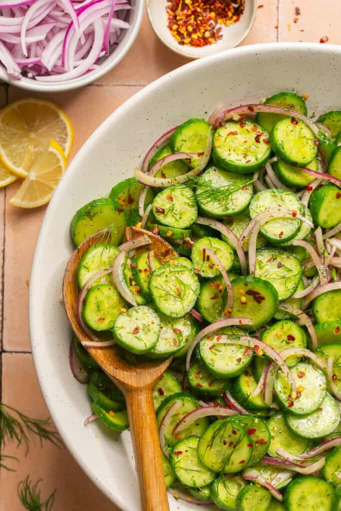 cucumber salad in white bowl with wooden spoon