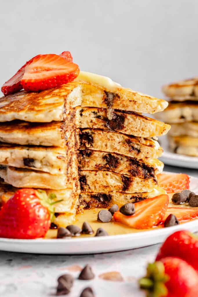 stack of chocolate chip pancakes, sliced, with strawberries and maple syrup