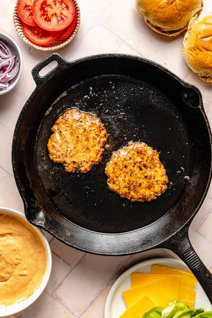 two ground turkey smash burger patties in cast iron skillet