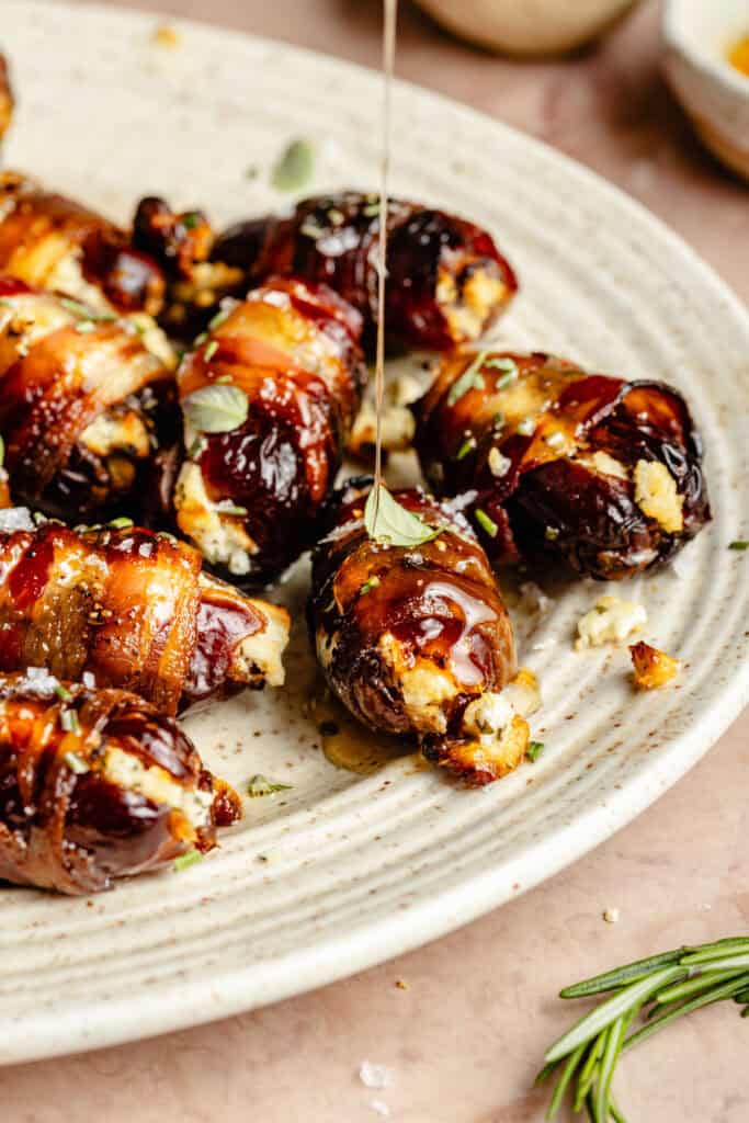 bacon wrapped dates on serving platter being drizzled with honey