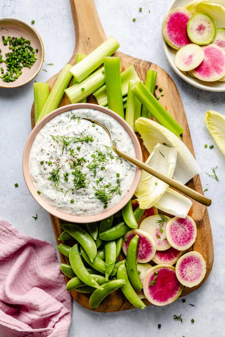 homemade ranch dressing in bowl with spoon surrounded by various veggies