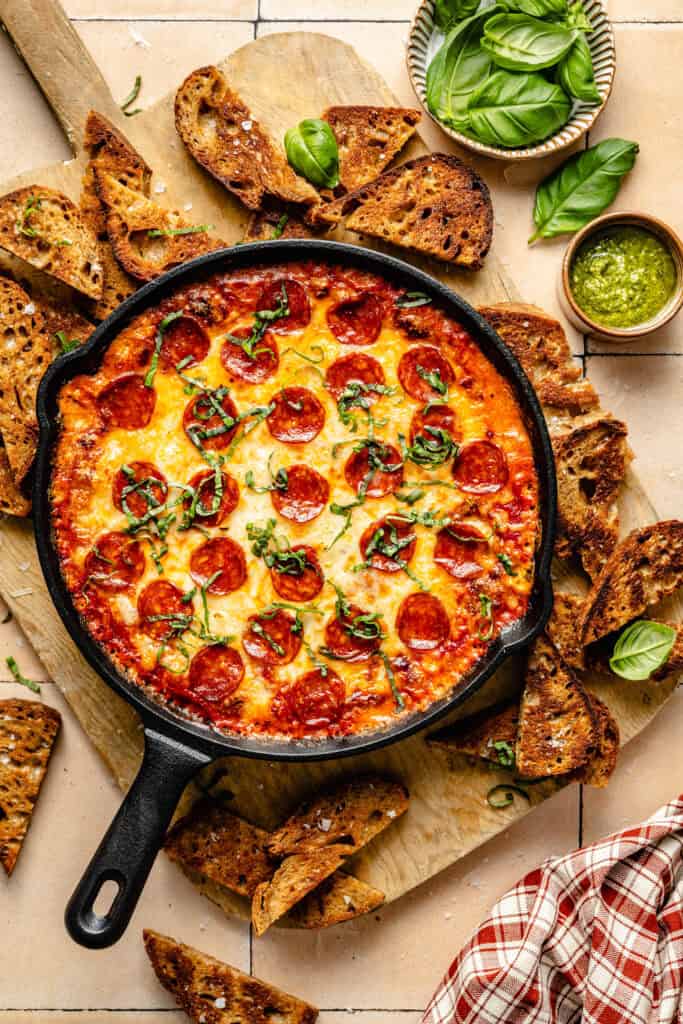 pizza dip topped with basil and surrounded by crusty bread 