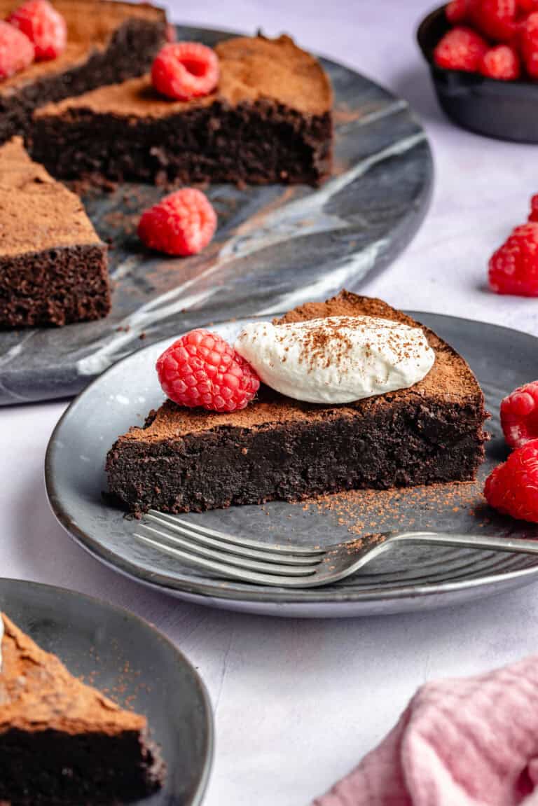 slice of chocolate cake on plate topped with whipped cream and berries