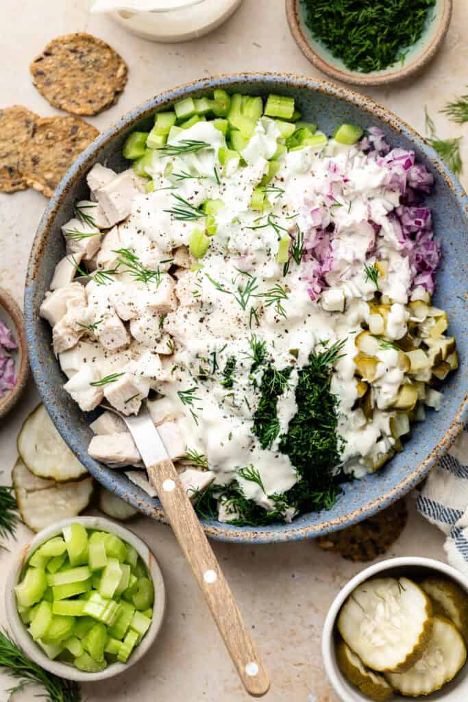 dressing poured over chicken salad ingredients in bowl