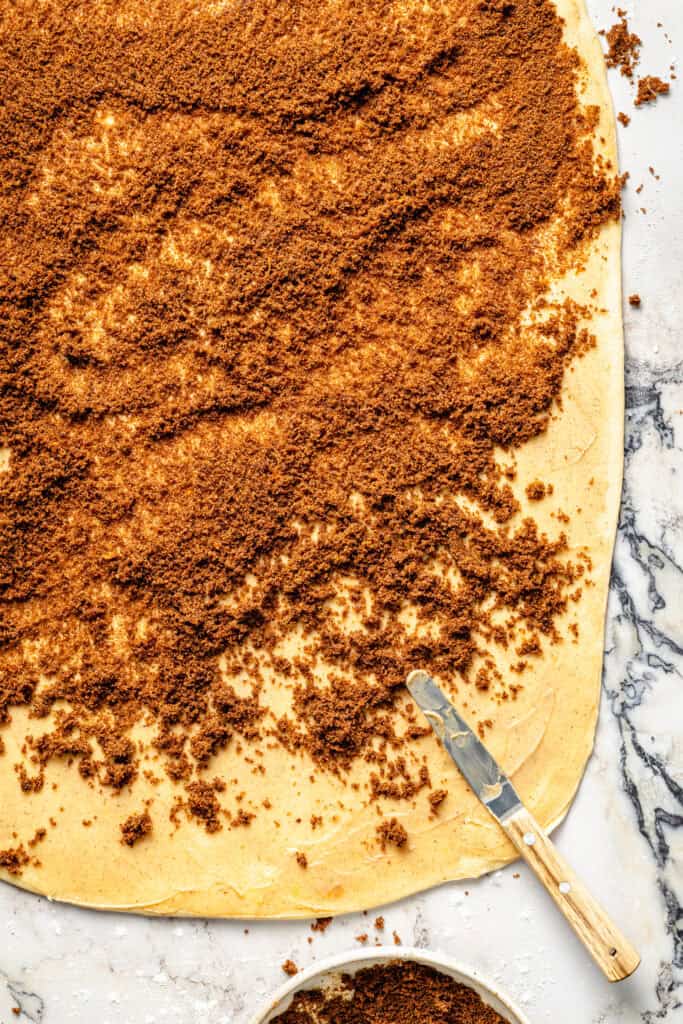 brown sugar being spread on cinnamon rolls