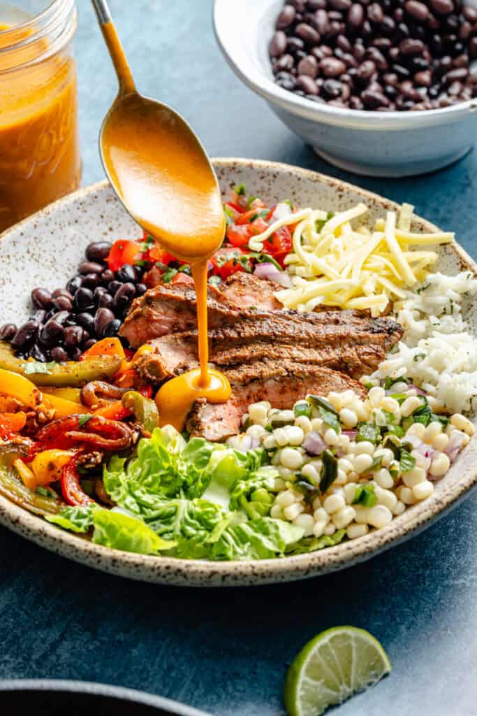 chipotle dressing being drizzled over steak bowl