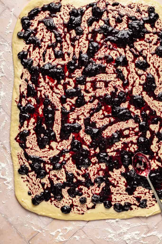 blueberry jam being spread over sweet roll dough