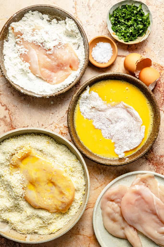 chicken cutlets being dredged in egg mixture