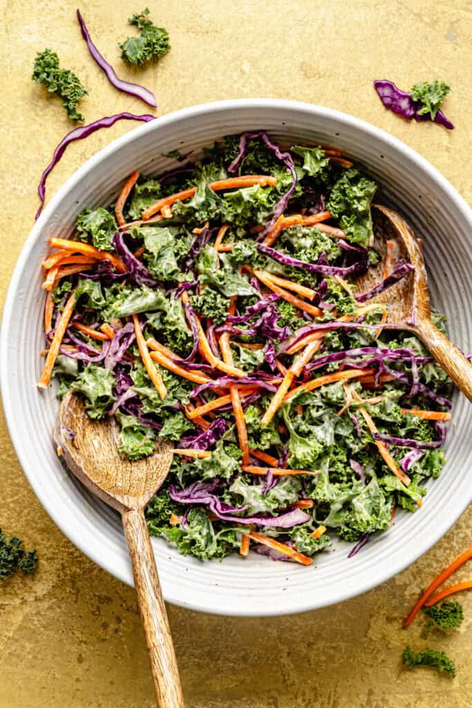 kale slaw in mixing bowl with wooden spoons