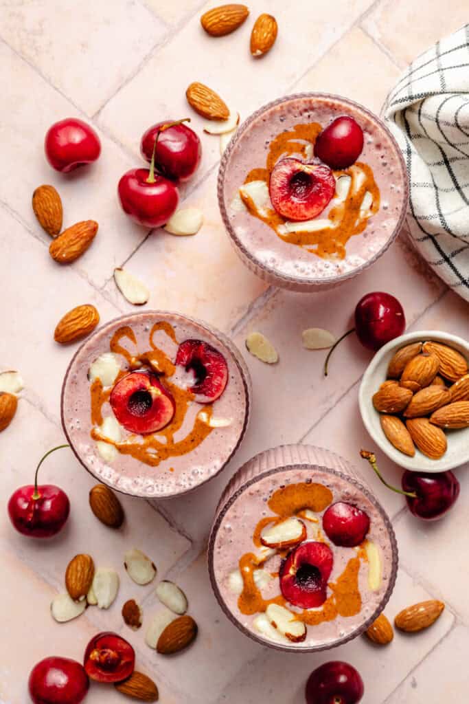 3 glasses of cherry almond smoothie topped with cherries, almond butter, and sliced almonds