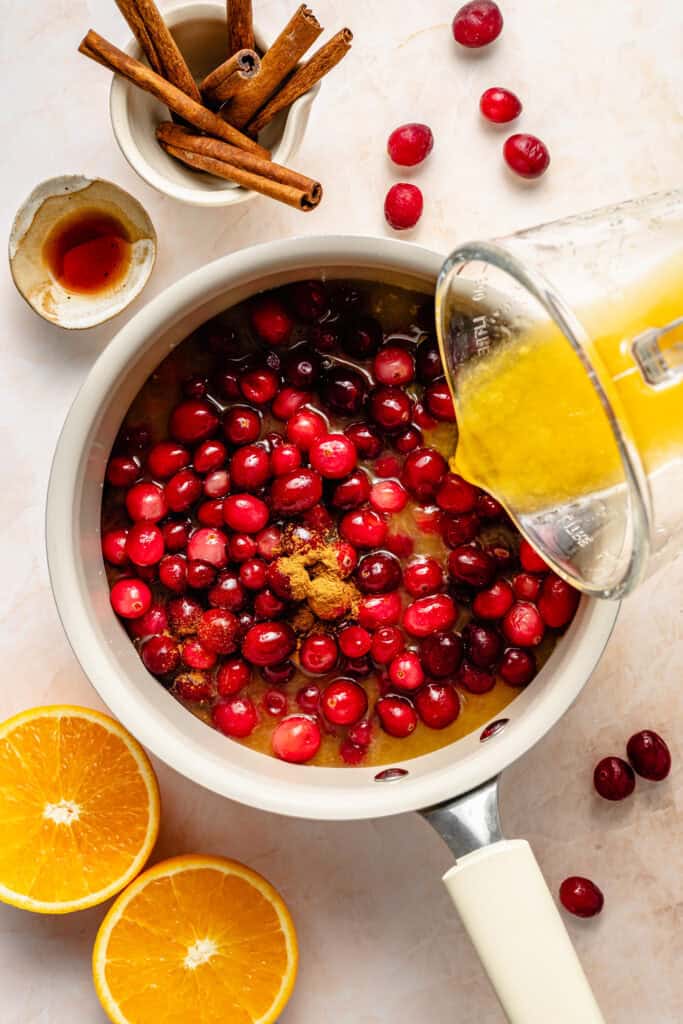 orange juice being poured over cranberries in pot