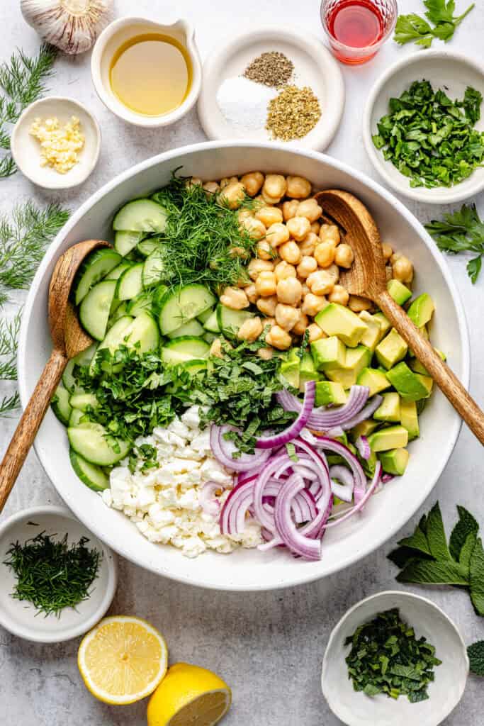 cucumber chickpea salad ingredients in mixing bowl with wooden spoon